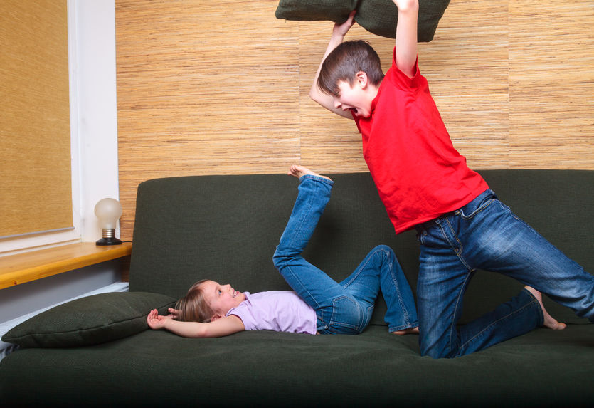 51293605 - brother and sister  wearing casual clothes  playing on a green sofa at home fighting with pillows